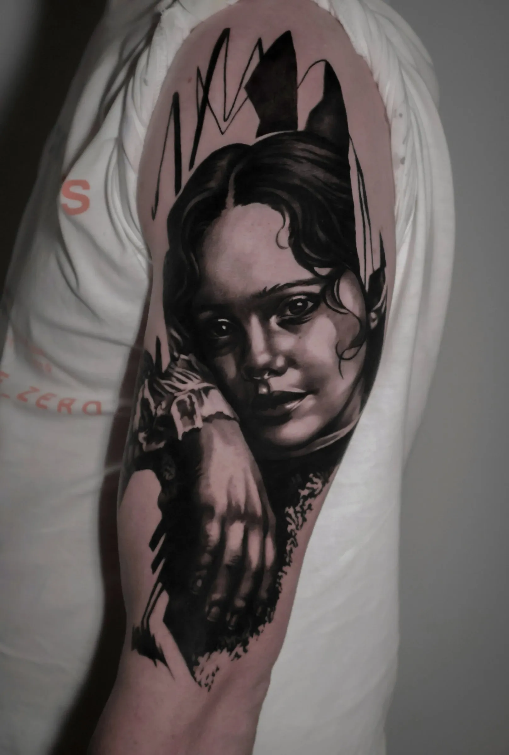 Reality is painted: realistisch zwart-grijs portret van een meisje met donker haar en een hand onder de kin, tussen abstracte zwarte vormen, op de bovenarm