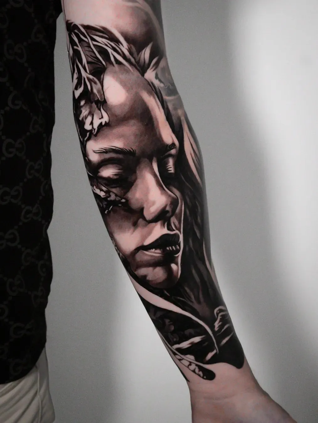 Power in stillness: surreal black and grey portrait of a woman with closed eyes, surrounded by leaves and organic shapes, on the forearm