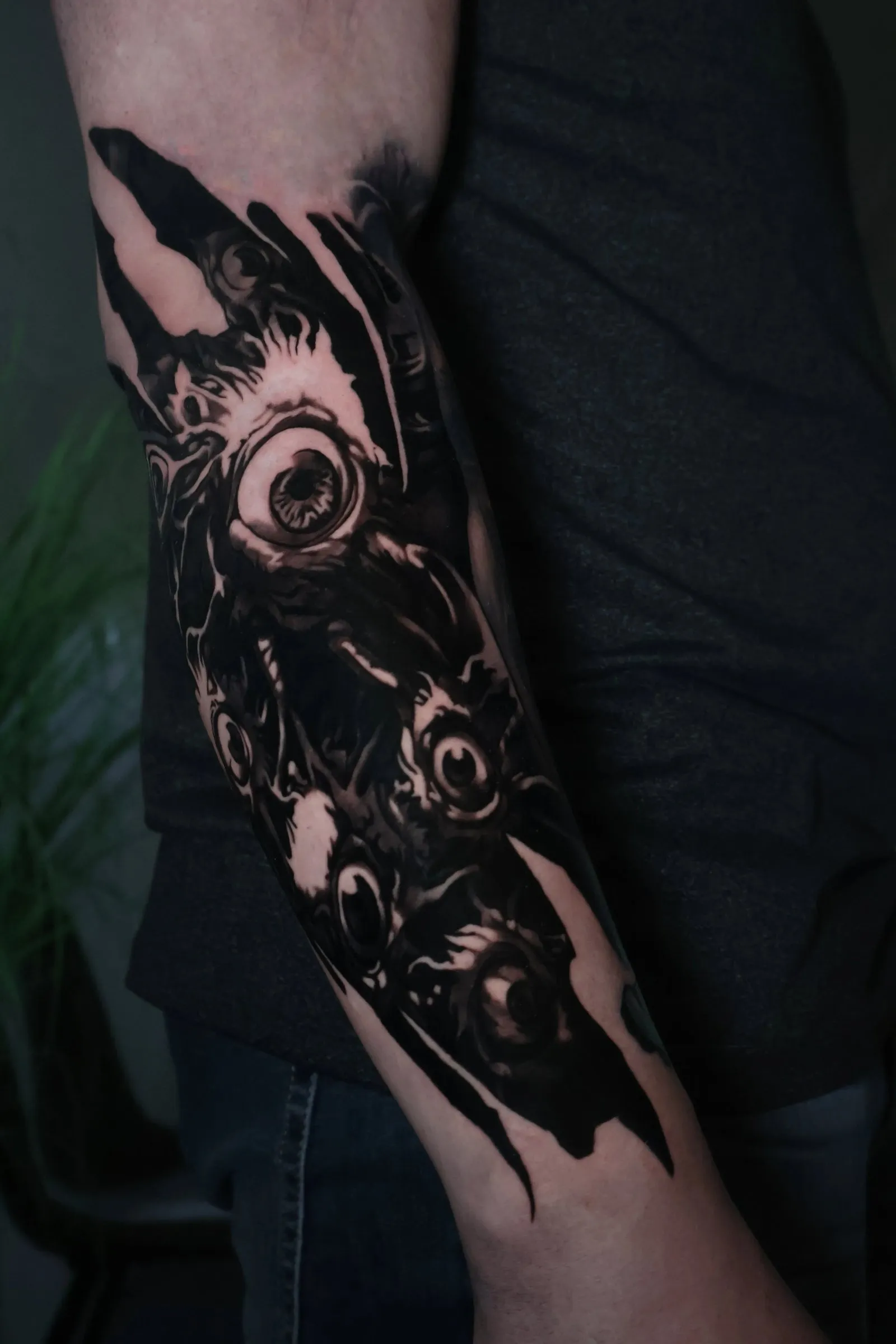 Quiet mind, heavy soul, dark ink: surreal sci-fi horror piece in dark black and grey with staring eyes, covering the full forearm