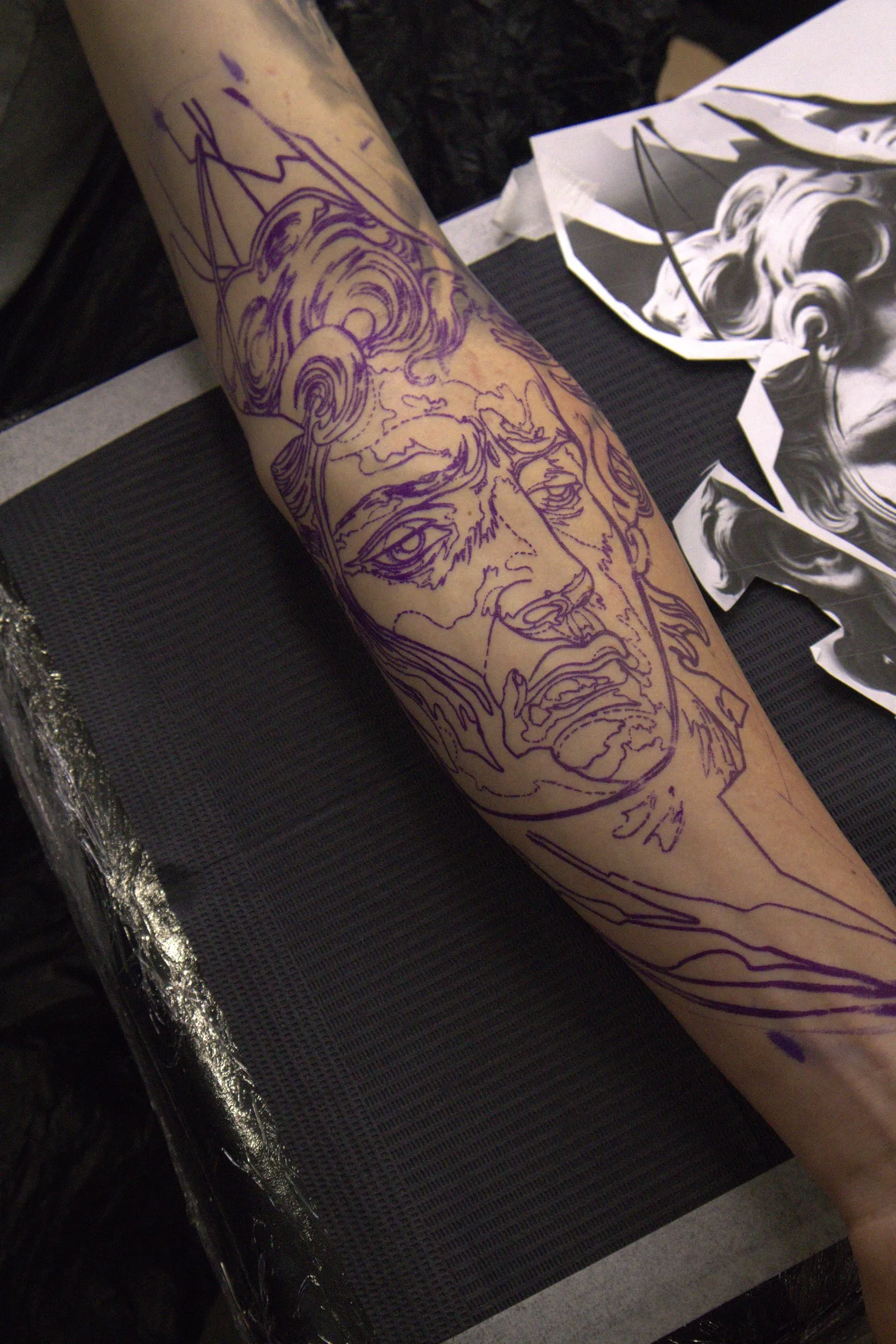Abstract mind, sharp lines: het paarse stencil van het beeldengezicht op de onderarm, met de afgedrukte referenties ernaast